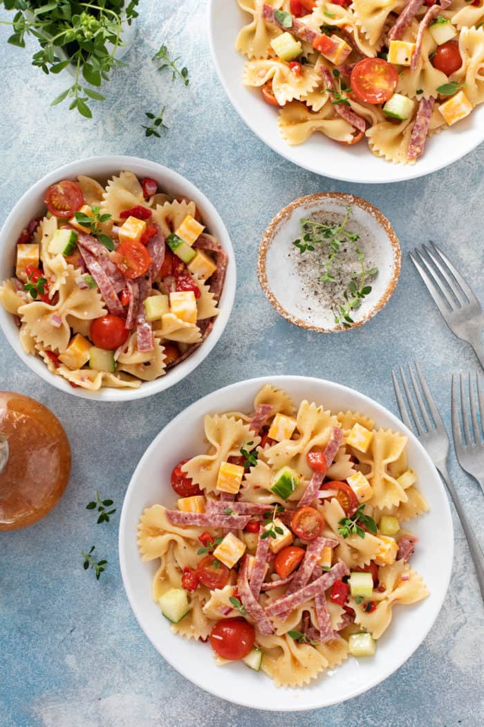 Three small bowls filled with italian pasta salad on a blue countertop.