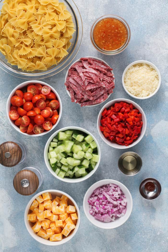 Ingredients for italian pasta salad arranged on a blue countertop.
