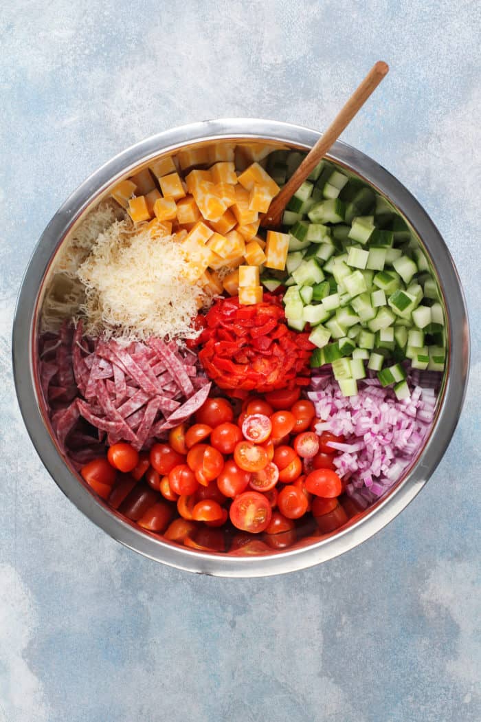 Veggies and cheese for italian pasta salad in a metal mixing bowl.