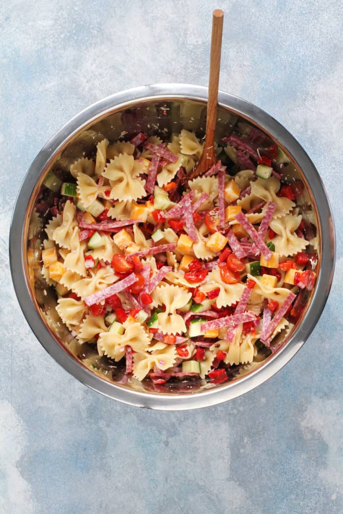 Italian pasta salad being mixed in a metal mixing bowl.