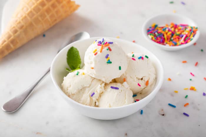 Scoops of vanilla no-churn ice cream in a white bowl, topped with rainbow sprinkles.