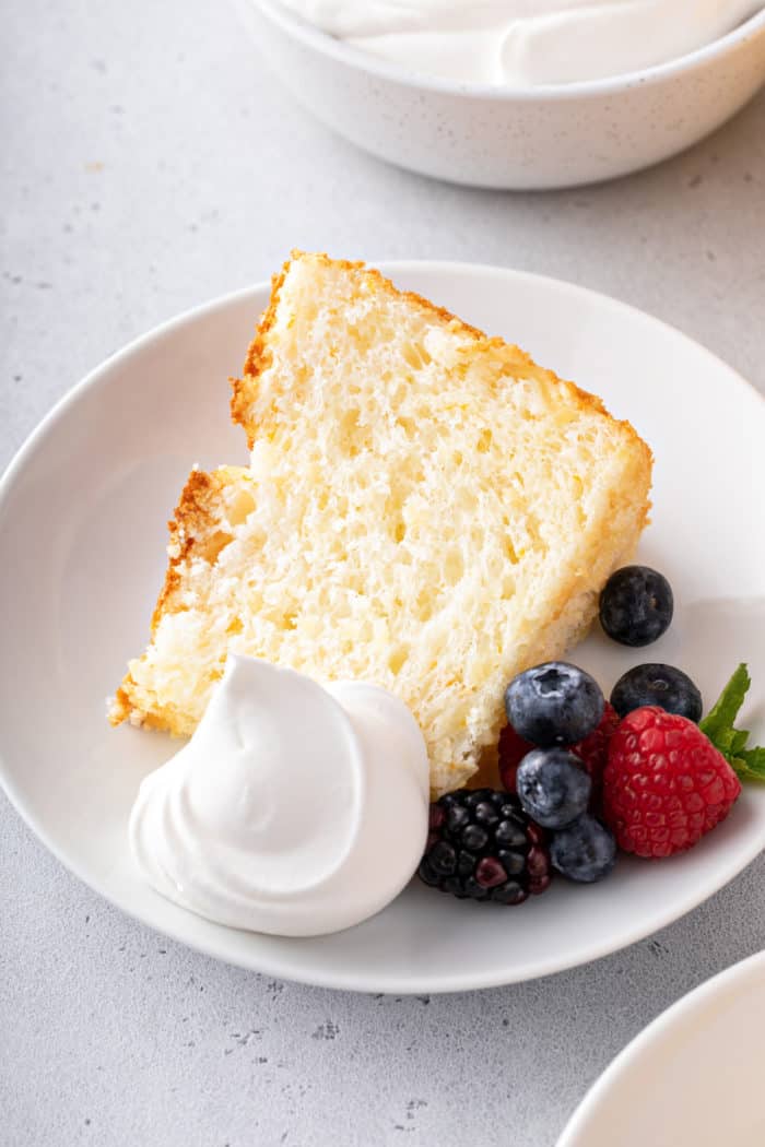 Plated slice of angel food cake, garnished with cool whip and berries.