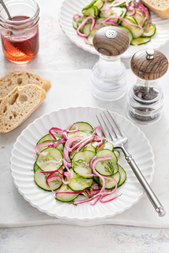 Cucumber salad on a white plate set next to slices of bread.