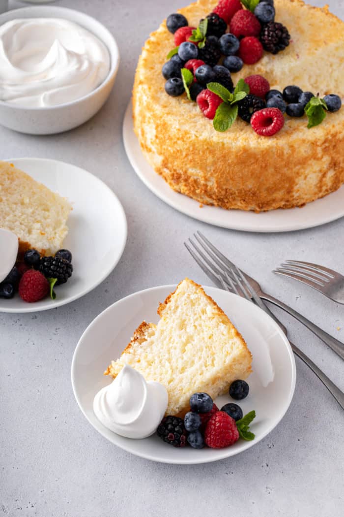 Two white plates with slices of pineapple angel food cake, with the whole cake in the background.