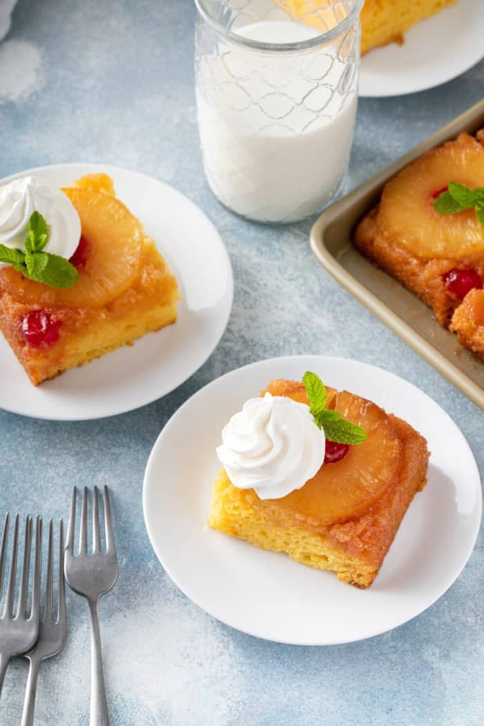 Two white plates with slices of easy pineapple upside down cake, each topped with a dollop of whipped cream.