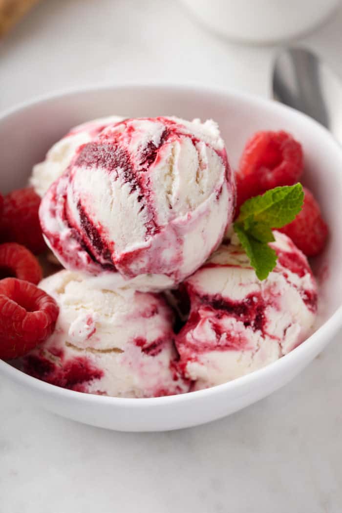 Scoops of raspberry swirl ice cream in a white bowl, garnished with fresh raspberries.