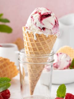 Waffle cone with a scoop of strawberry swirled ice cream propped up in a glass jar.