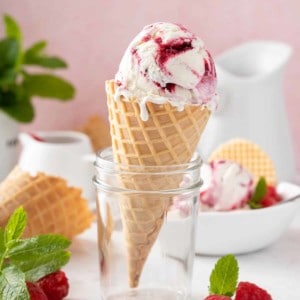 Waffle cone with a scoop of strawberry swirled ice cream propped up in a glass jar.