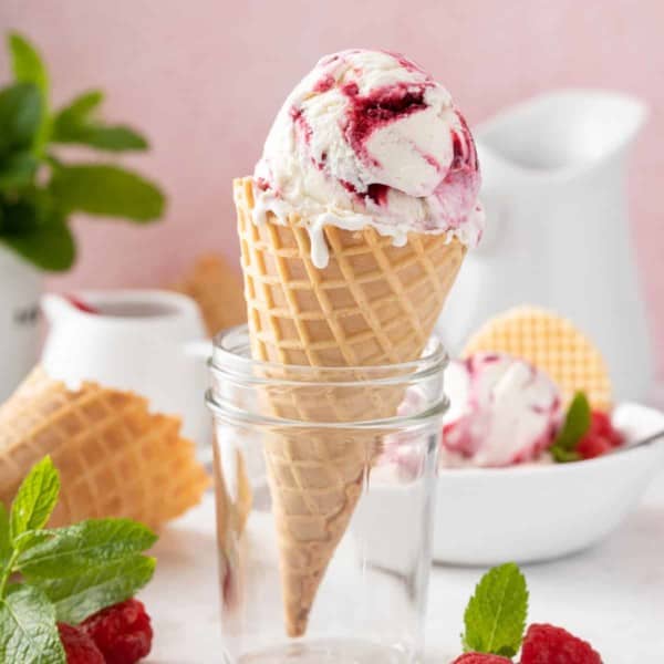 Waffle cone with a scoop of strawberry swirled ice cream propped up in a glass jar.