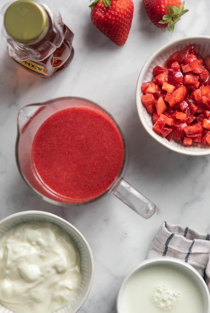 Ingredients for strawberry popsicles arranged on a marble countertop.