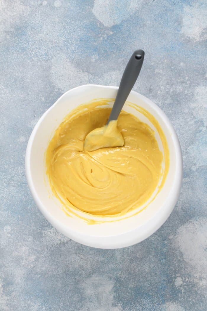 Yellow cake batter being stirred with a spatula in a white bowl.