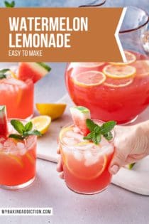 Hand holding up a glass of watermelon lemonade. More glasses and a pitcher of the lemonade are in the background. Text overlay includes recipe name.