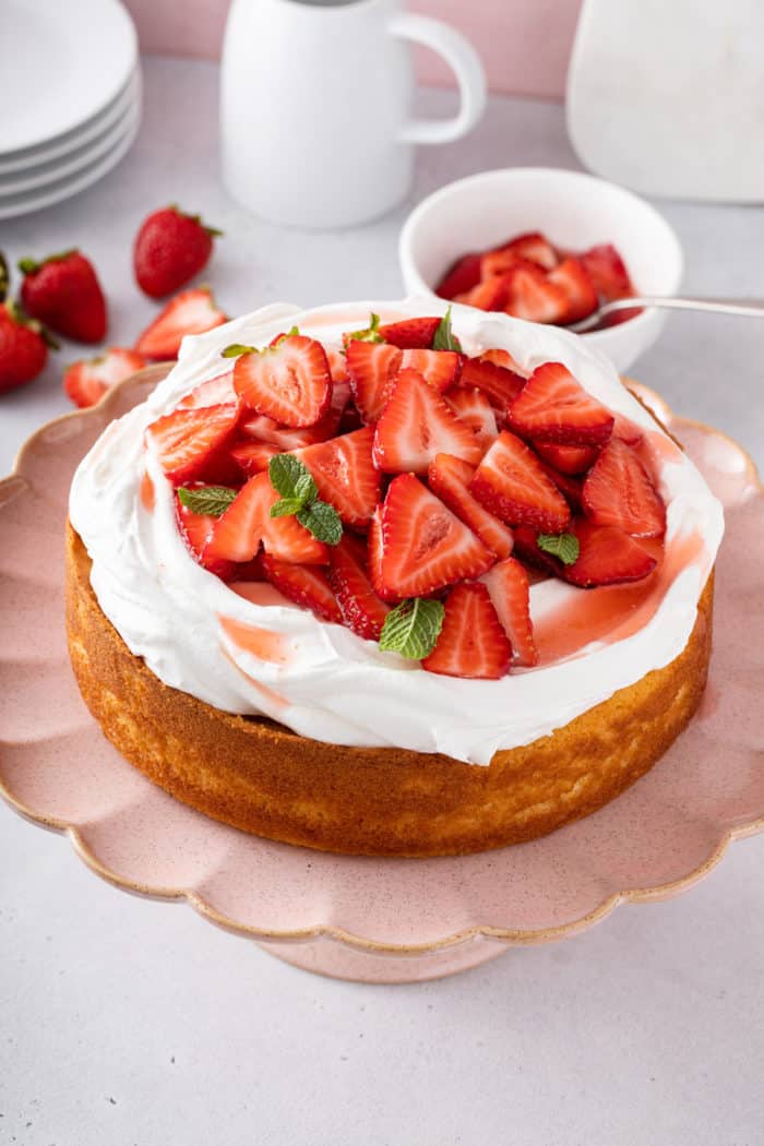 Strawberry shortcake topped with whipped cream and sliced strawberries on a pink cake plate.