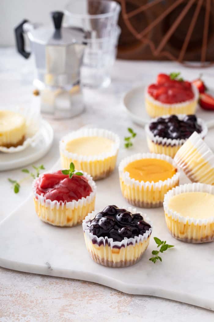 Several mini cheesecakes with assorted fruit toppings scattered on a marble board.