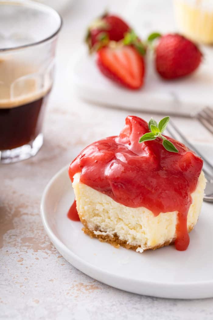 Plated mini cheesecake topped with strawberry pie filling. A bite has been taken from the cheesecake.