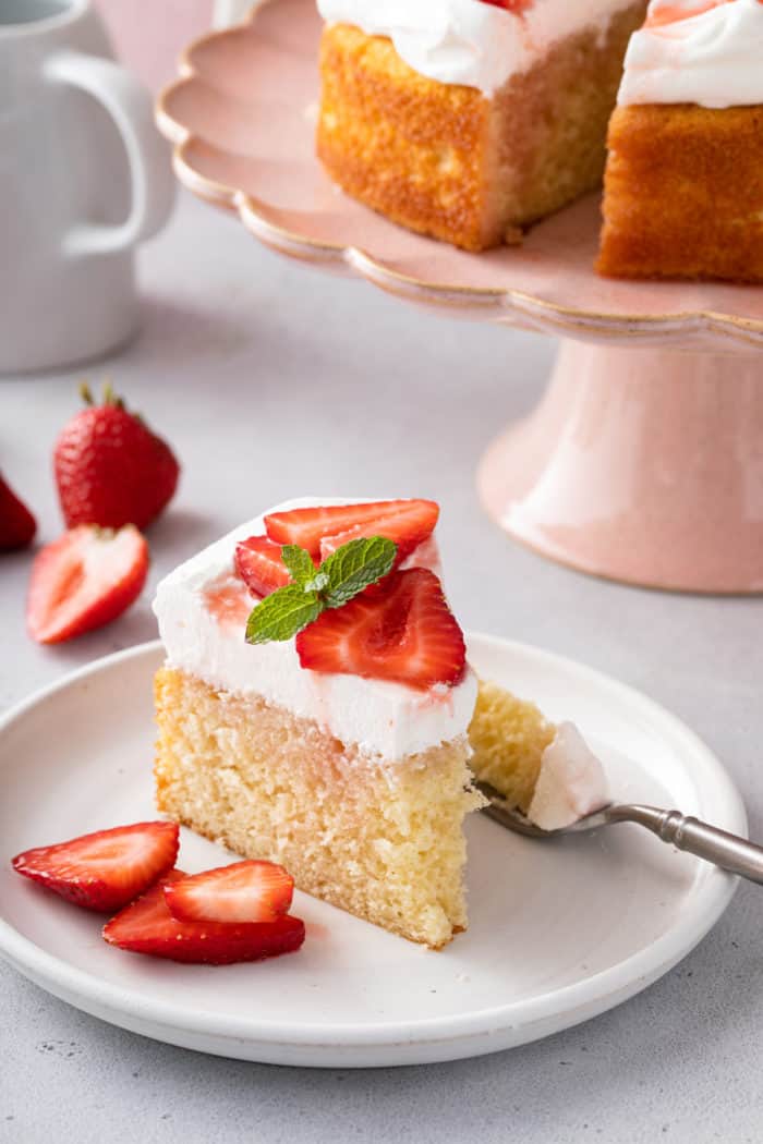 Slice of strawberry shortcake with a bite taken out of it on a white plate.