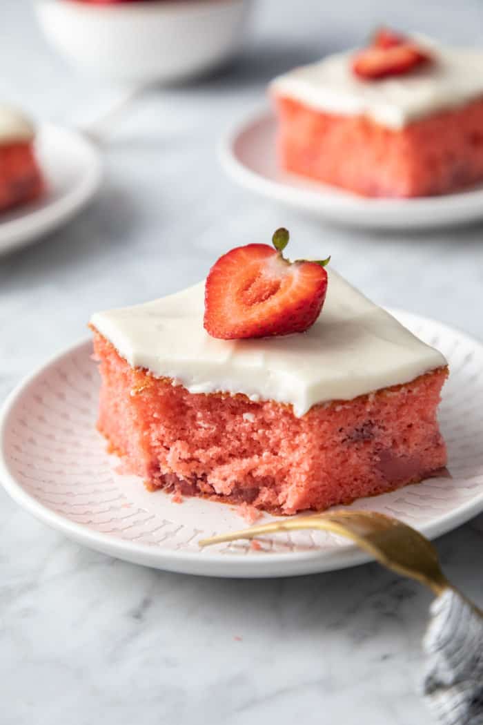 Slice of strawberry cake on a white plate. A bite has been taken from one corner of the cake.