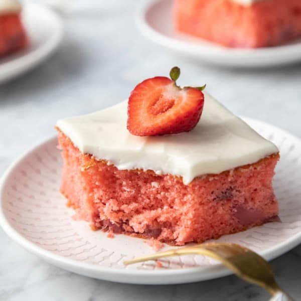 White plate with a slice of strawberry cake. A fork rests on the edge of the plate and a bite has been taken from the cake.