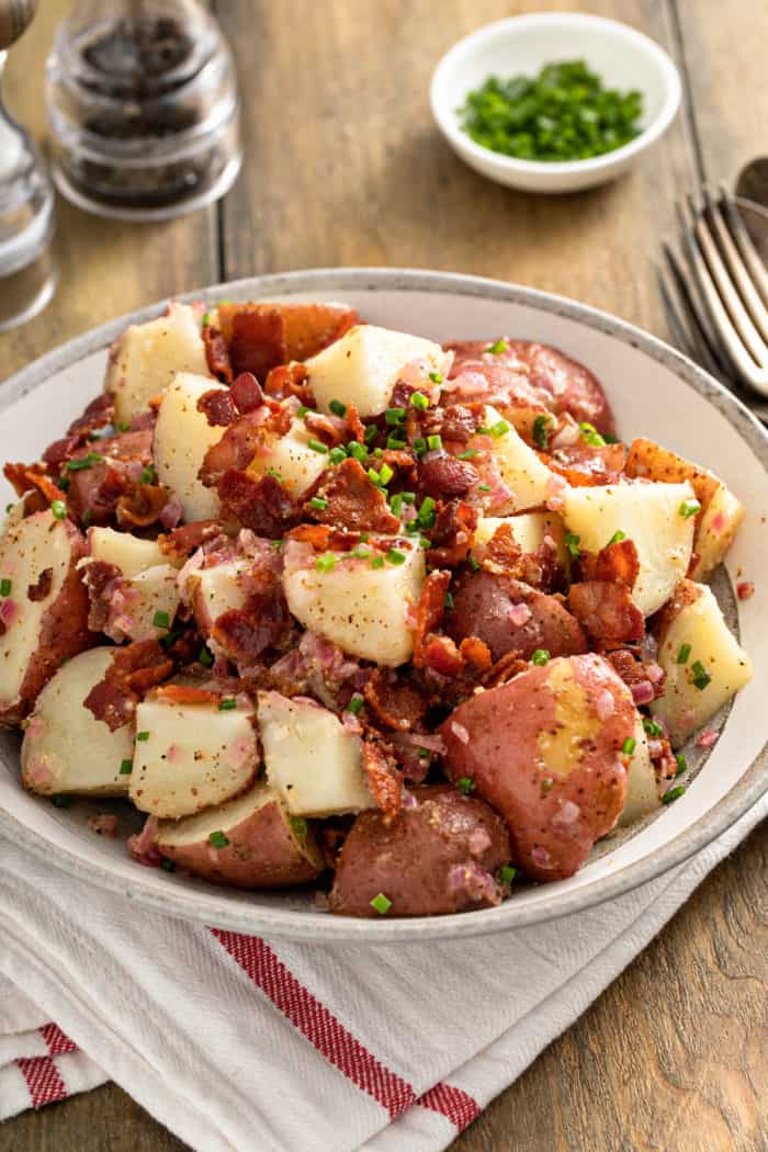 German potato salad, garnished with bacon and chives, in a large serving bowl.