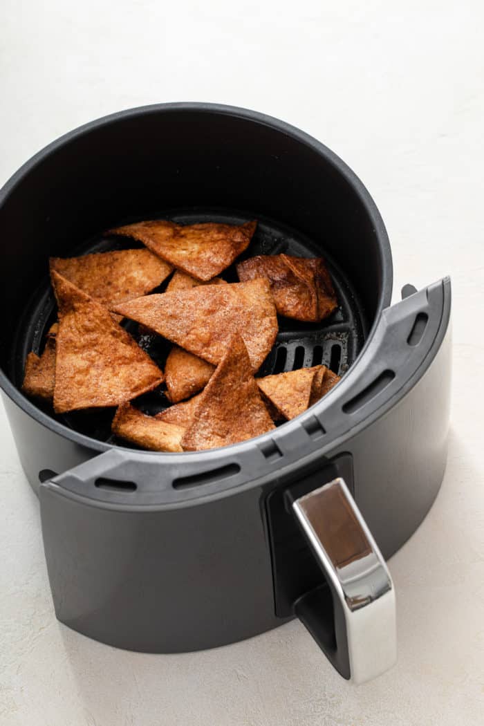 Cooked cinnamon tortilla chips in the basket of an air fryer.