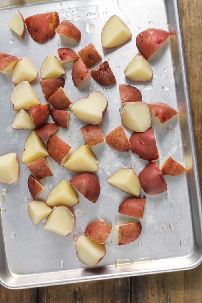 Cooked red potatoes spread out onto a metal sheet pan.