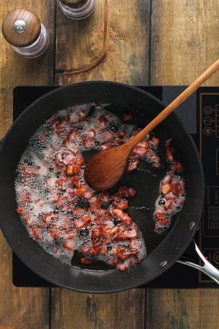 Bacon being cooked in a black skillet.