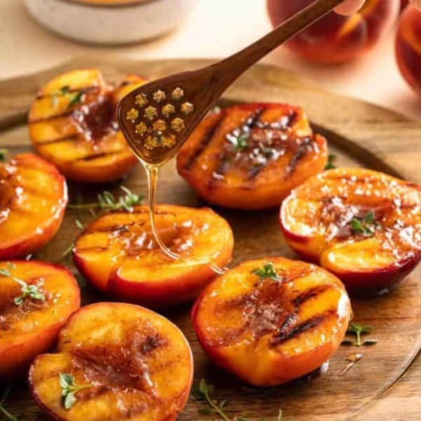 Honey being drizzled over grilled peach halves arranged on a wooden platter.