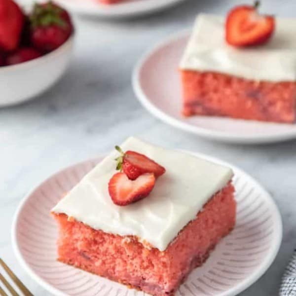 Three plates, each holding a slice of easy strawberry cake garnished with halved strawberries.