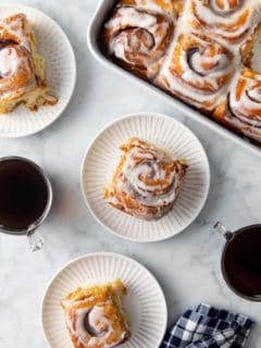 Three white plates with tiktok cinnamon rolls set on a marble countertop next to a baking dish of cinnamon rolls.