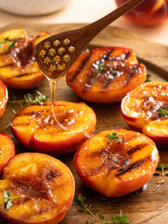 Honey being drizzled over grilled peaches.
