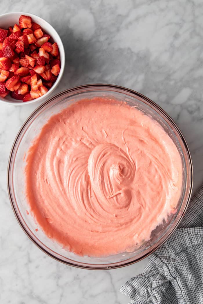 Easy strawberry cake batter in a glass mixing bowl next to a bowl of diced strawberries.