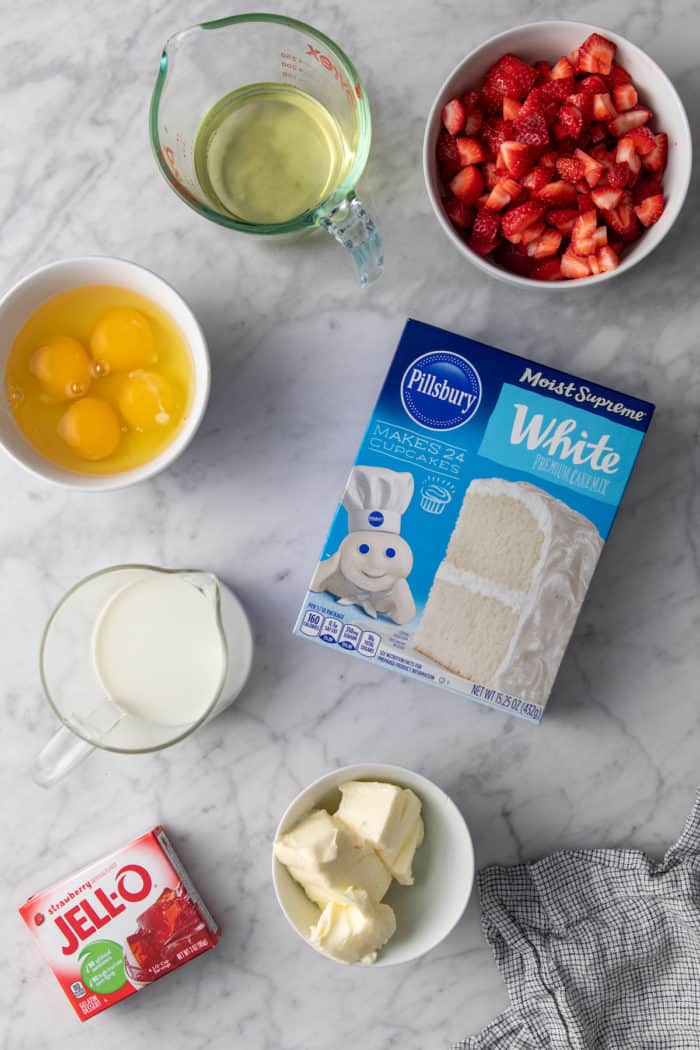 Ingredients for easy strawberry cake arranged on a marble countertop.