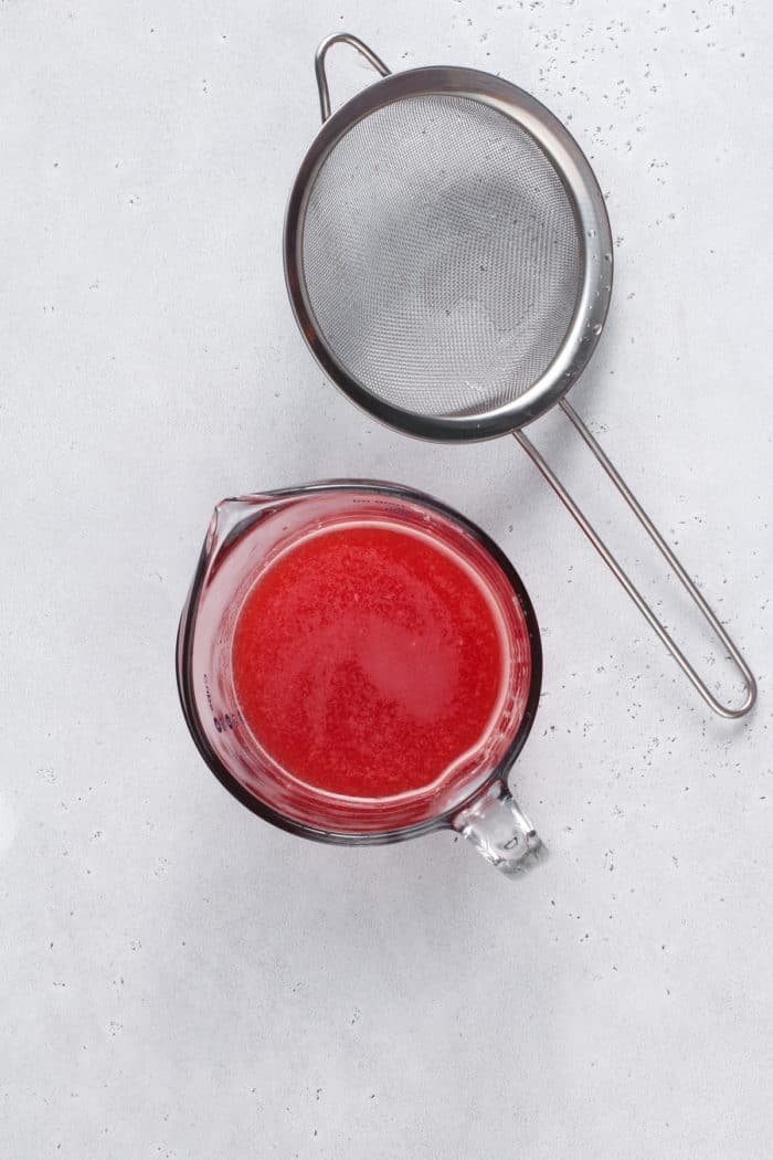 Strained watermelon juice in a glass measuring cup, set on a gray countertop.
