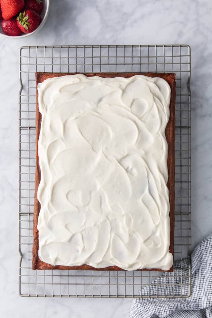 Frosted strawberry cake set on a wire cooling rack on a marble counter.