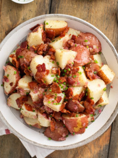 Overhead view of german potato salad in a serving bowl, set on a wooden table.