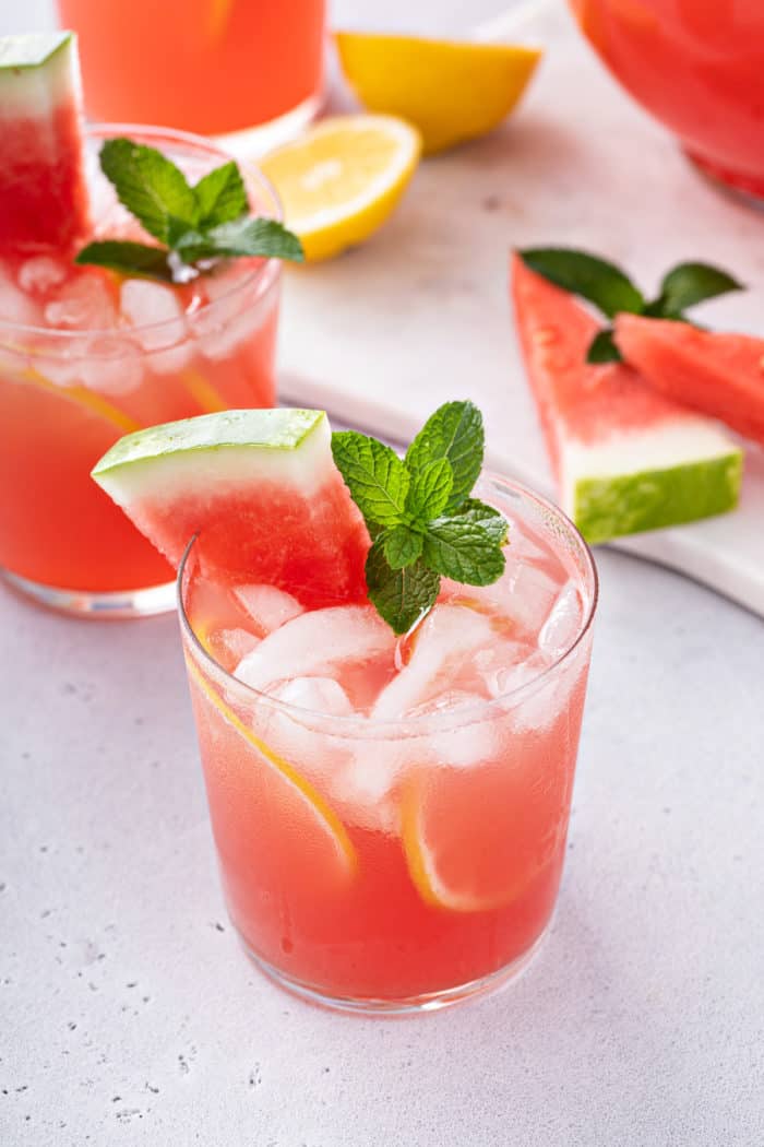 Glass of watermelon lemonade garnished with a piece of watermelon and a sprig of mint.