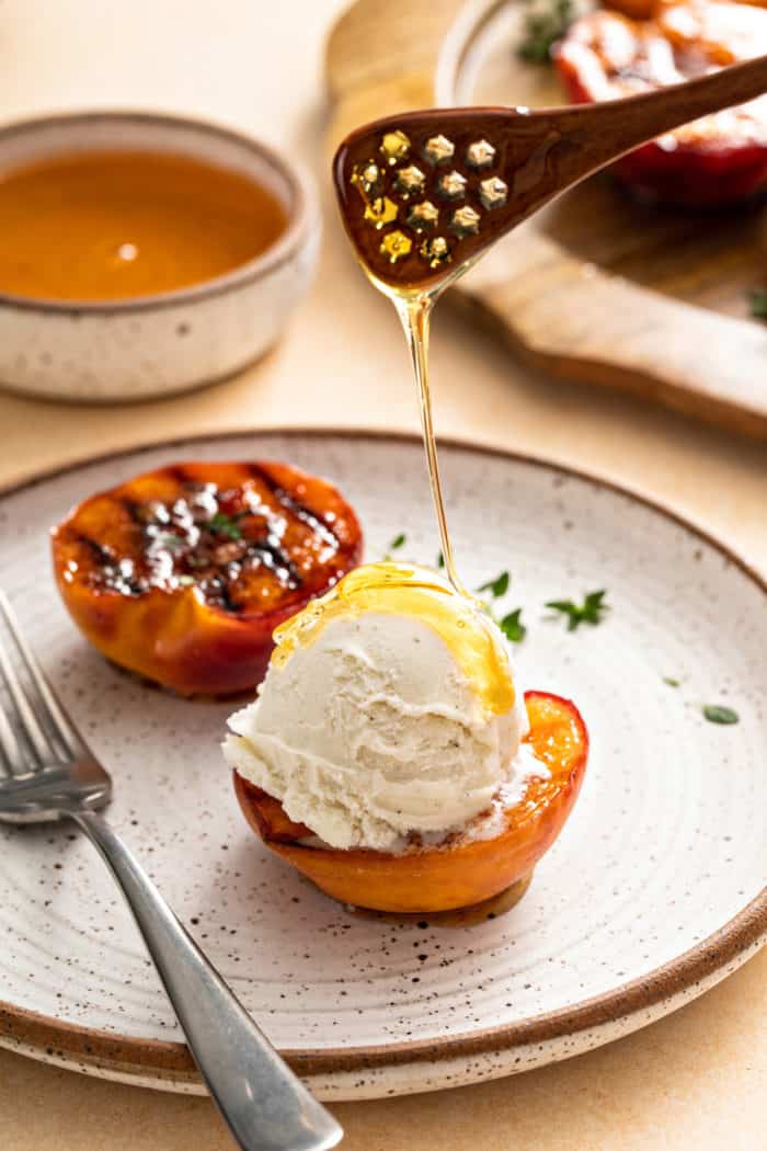 Honey being drizzled over ice cream on a grilled peach half.