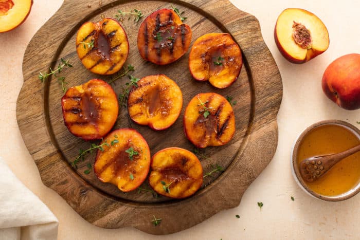 Grilled peach halves set on a wooden platter.