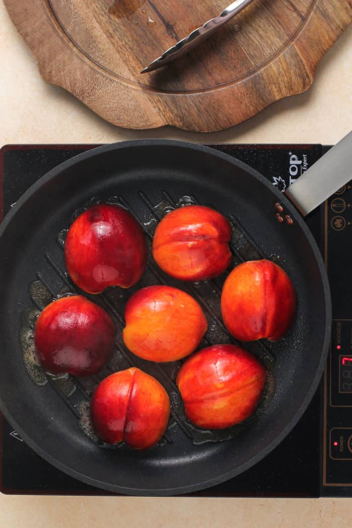 Peach halves set cut-side down in a grill pan.