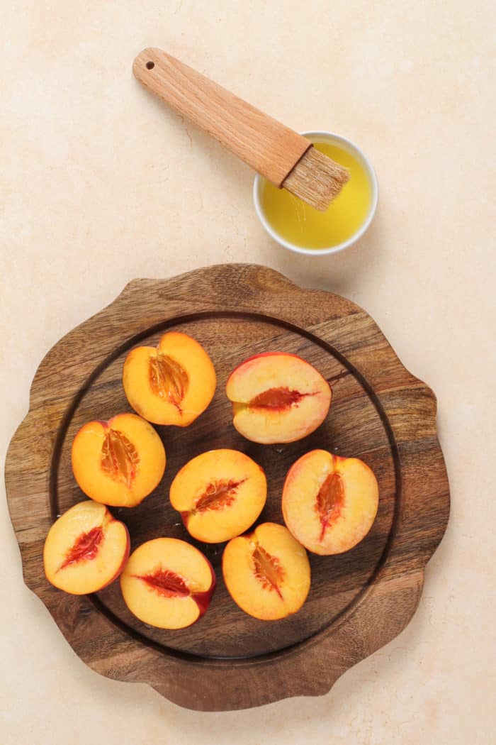 Halved peaches on a wooden plater next to a bowl of melted butter.