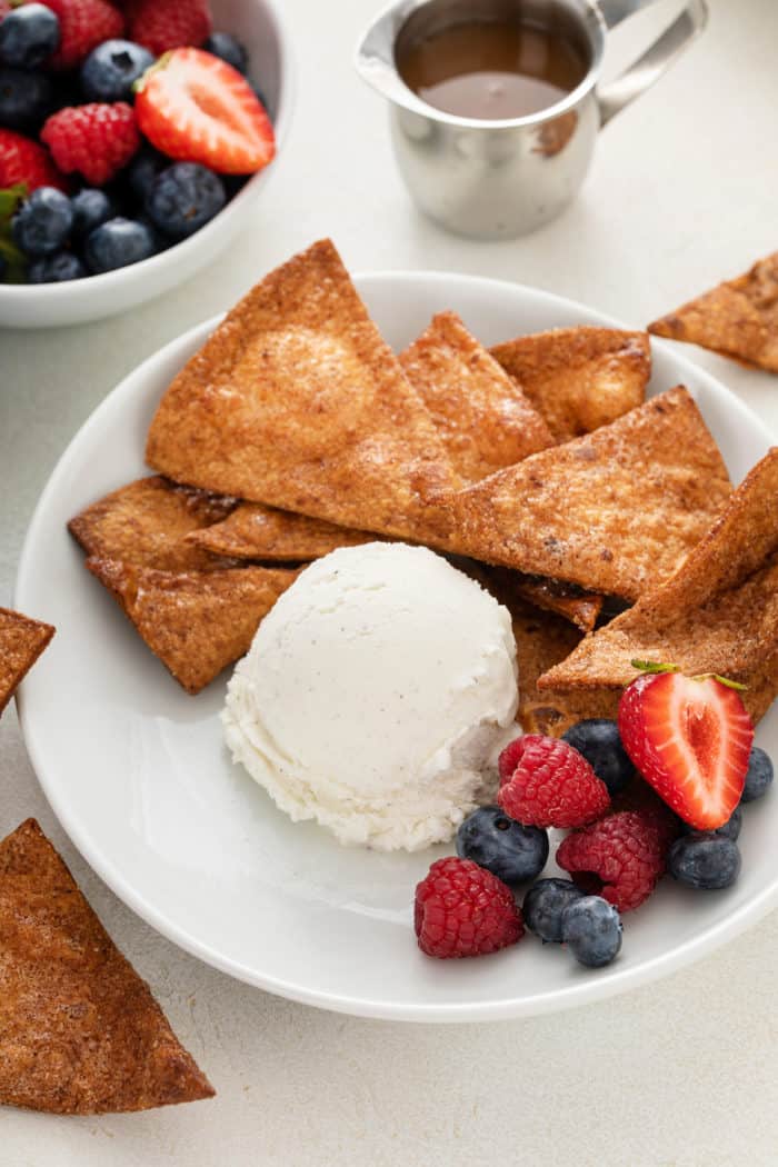 Cinnamon tortilla chips in a bowl alongside a scoop of vanilla ice cream and fresh berries.