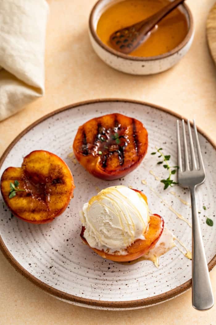 Pottery plate with 3 grilled peach halves. A scoop of ice cream is on one of them.