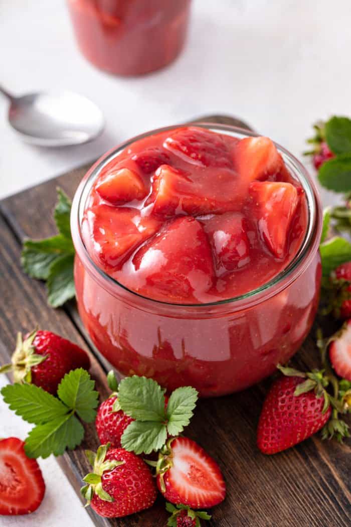 Glass jar filled with strawberry pie filling, surrounded by fresh strawberries.