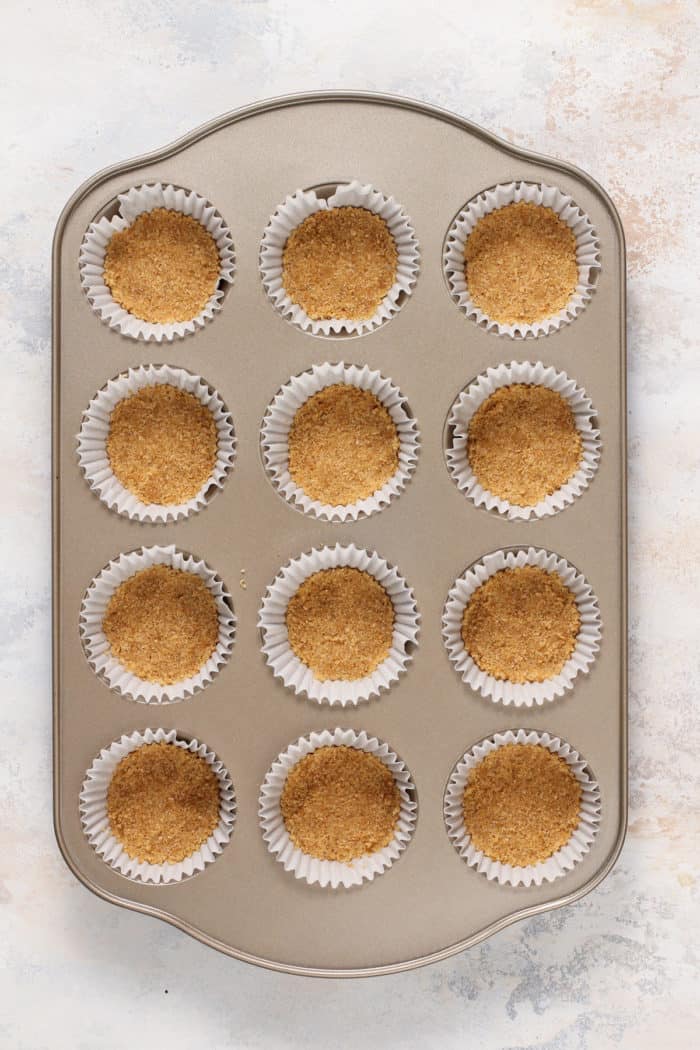 Crusts for mini cheesecakes in paper-lined muffin cups.