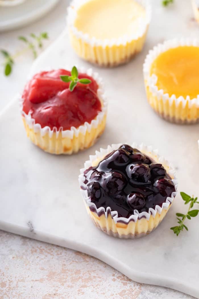Two mini cheesecakes, topped with strawberry pie filling and blueberry pie filling, set on a marble board.