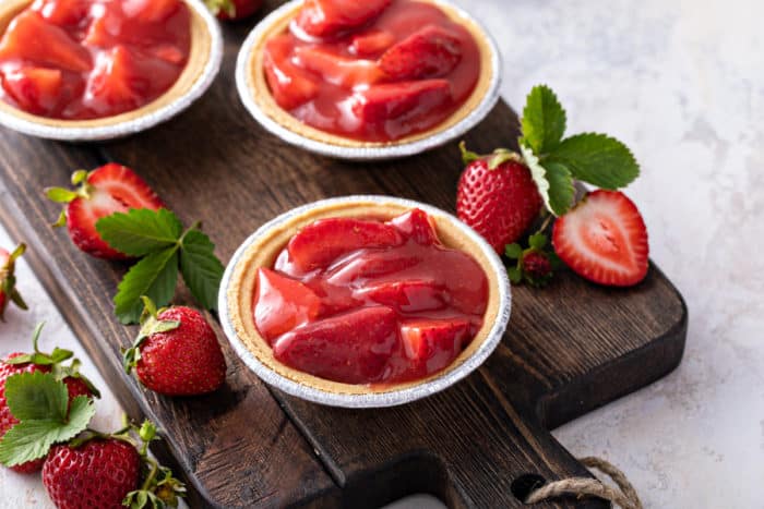 Strawberry pie filling in mini graham cracker crusts, set on a wooden board.