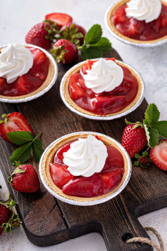 Mini strawberry pies in graham cracker crusts topped with whipped cream.