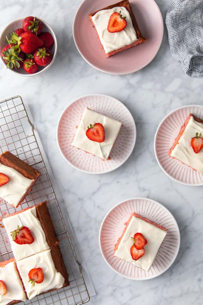 Four plated slices of easy strawberry cake arranged on a marble countertop next to the sliced strawberry cake.