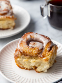 Close up of a cinnamon roll with heavy cream on a white plate.