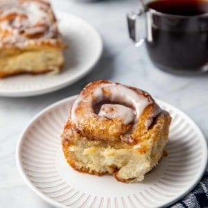 Close up of a cinnamon roll with heavy cream on a white plate.